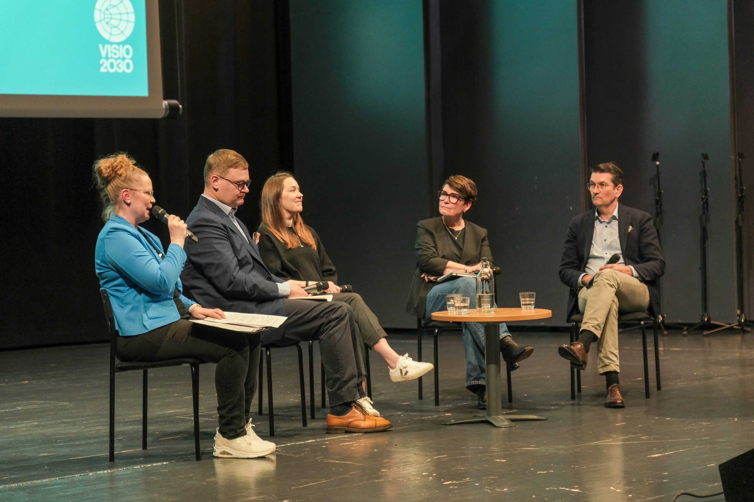 Viisi ihmistä istuu lavalla paneelikeskustelussa